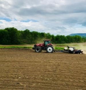 A farmer plants their corn using no-till. A red tractor pulls a no-till corn planter across dark brown soil on an overcast day.